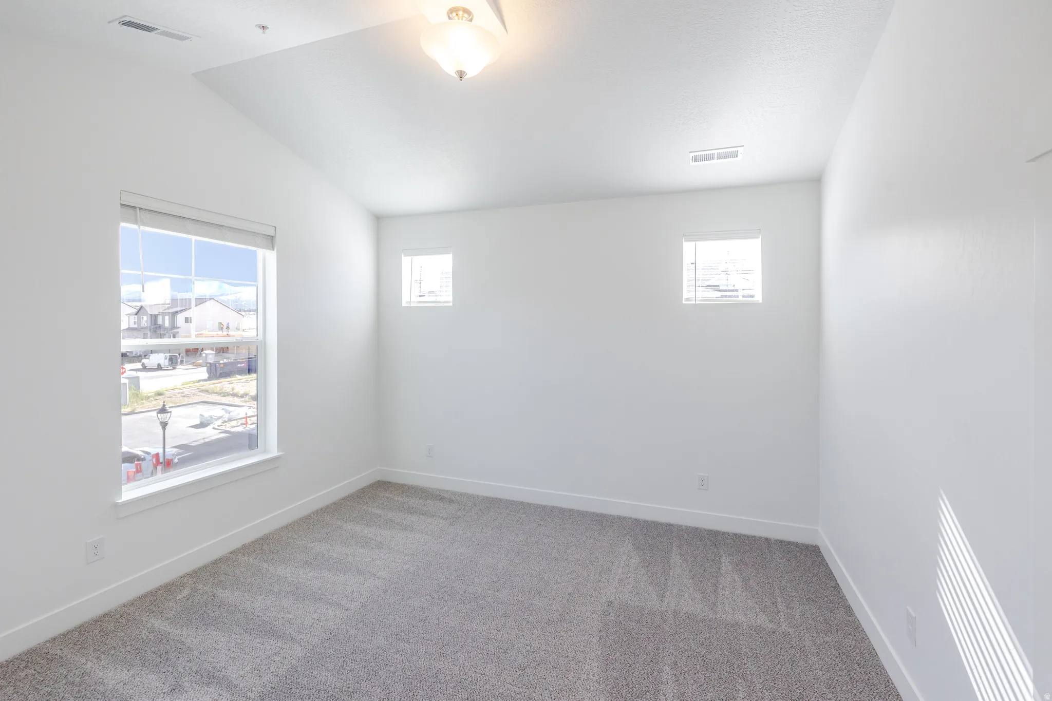 Carpeted room featuring a vaulted ceiling, multiple windows, and a flush-mount ceiling fixture