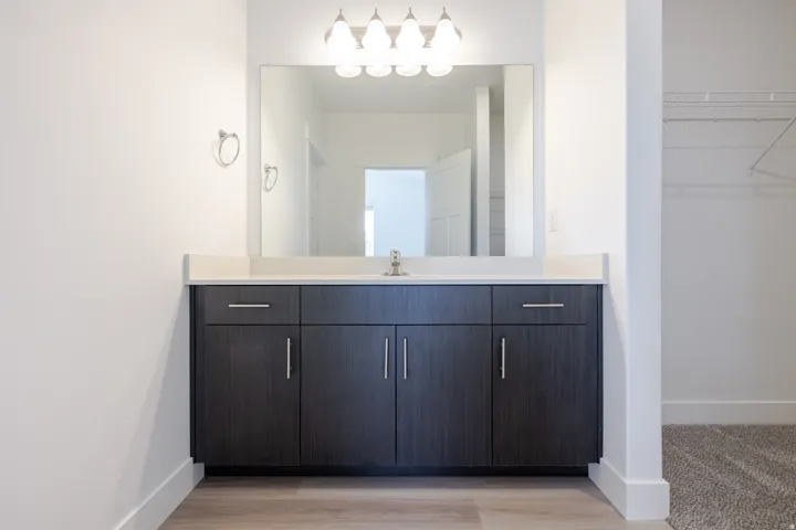 Wood-finish vanity with a light-toned countertop, undermount sink, and a large wall-mounted mirror