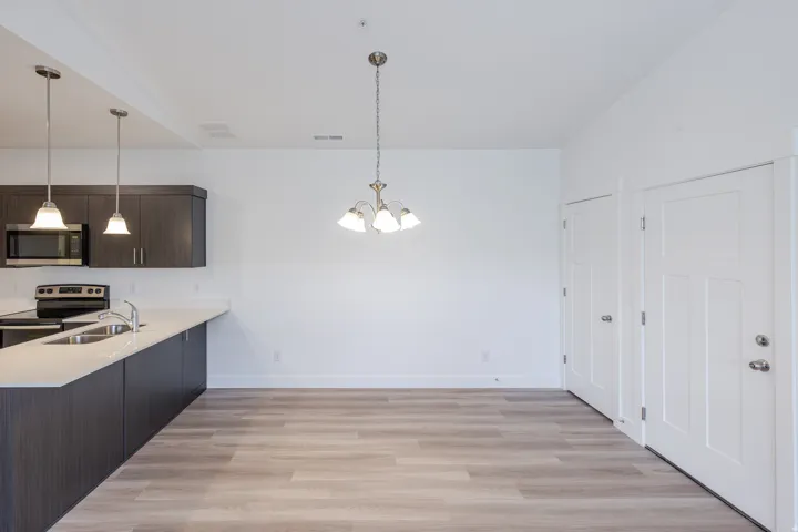 Open-concept living space featuring wood-finish flooring, dark wood-finish cabinetry, stainless steel appliances, and white countertops