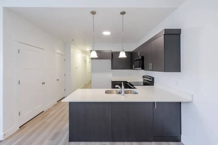 Kitchen island with dual basin sink, light-toned countertops, dark wood-finish cabinetry, and stainless steel appliances