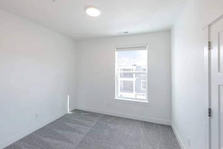 Recessed ceiling lighting, white walls, gray patterned carpet, single window with white trim, and a white paneled door