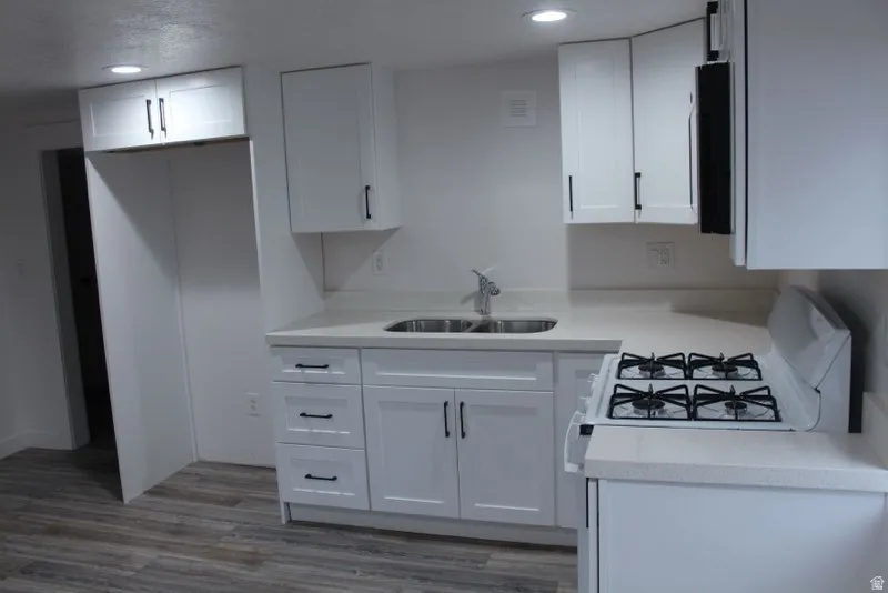Kitchen with white gas range oven, white cabinetry, light wood-style flooring, and recessed lighting