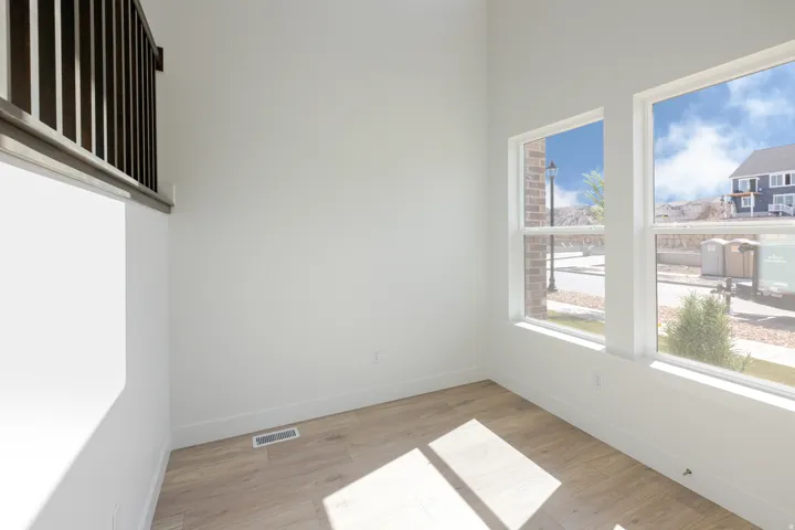 Bright interior featuring two large windows, wood-finish flooring, white baseboards, and a contemporary dark wood and metal railing