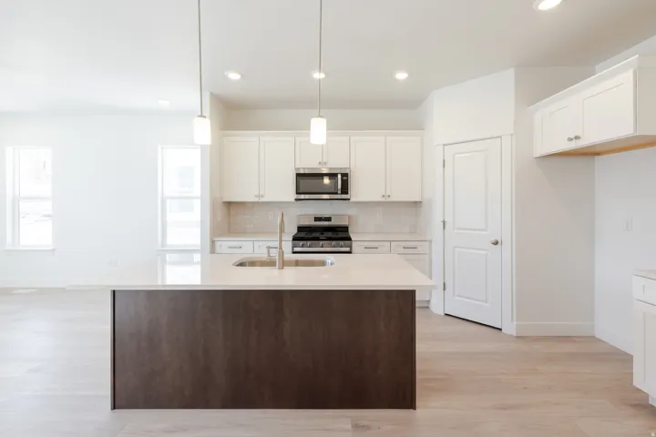 Contemporary kitchen featuring a large island with a composite countertop, stainless steel sink, and pendant lighting