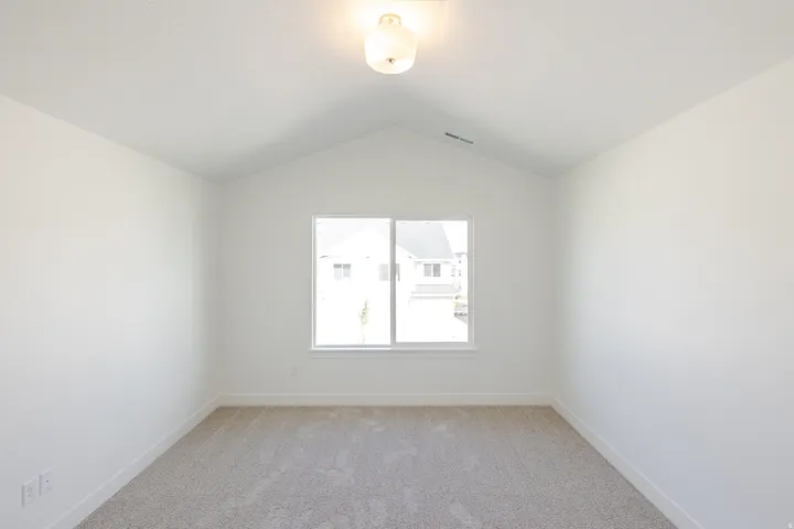 Vaulted ceiling bedroom featuring a neutral color palette, carpeted flooring, and a large window