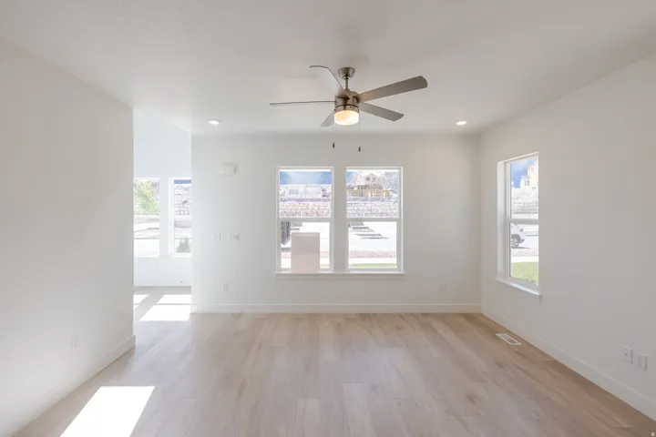 Bright living space featuring light wood-finish flooring, white walls, and a ceiling fan with integrated lighting