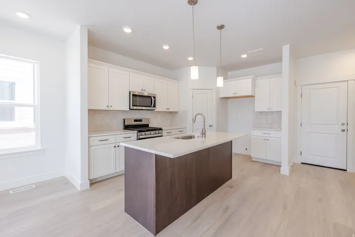 Open-concept kitchen featuring a central island with a sink, stainless steel appliances, white cabinetry, and light wood-finish flooring