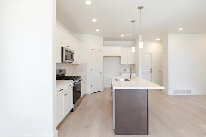 Kitchen featuring an island with a sink, white cabinetry, stainless steel appliances, light-toned wood-finish flooring, and recessed lighting