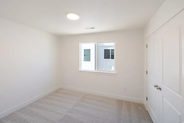 Room featuring light gray carpet flooring, white painted walls, a flush-mount ceiling light, a white framed window, and bi-fold closet doors