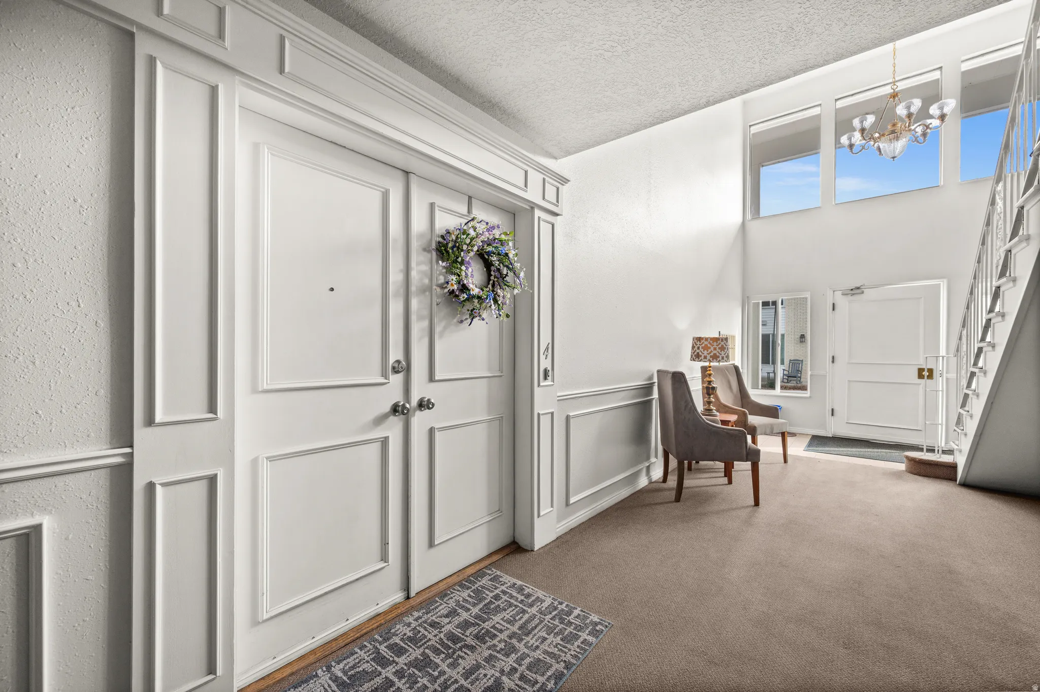 Carpeted foyer with a decorative wall, a chandelier, and a textured ceiling