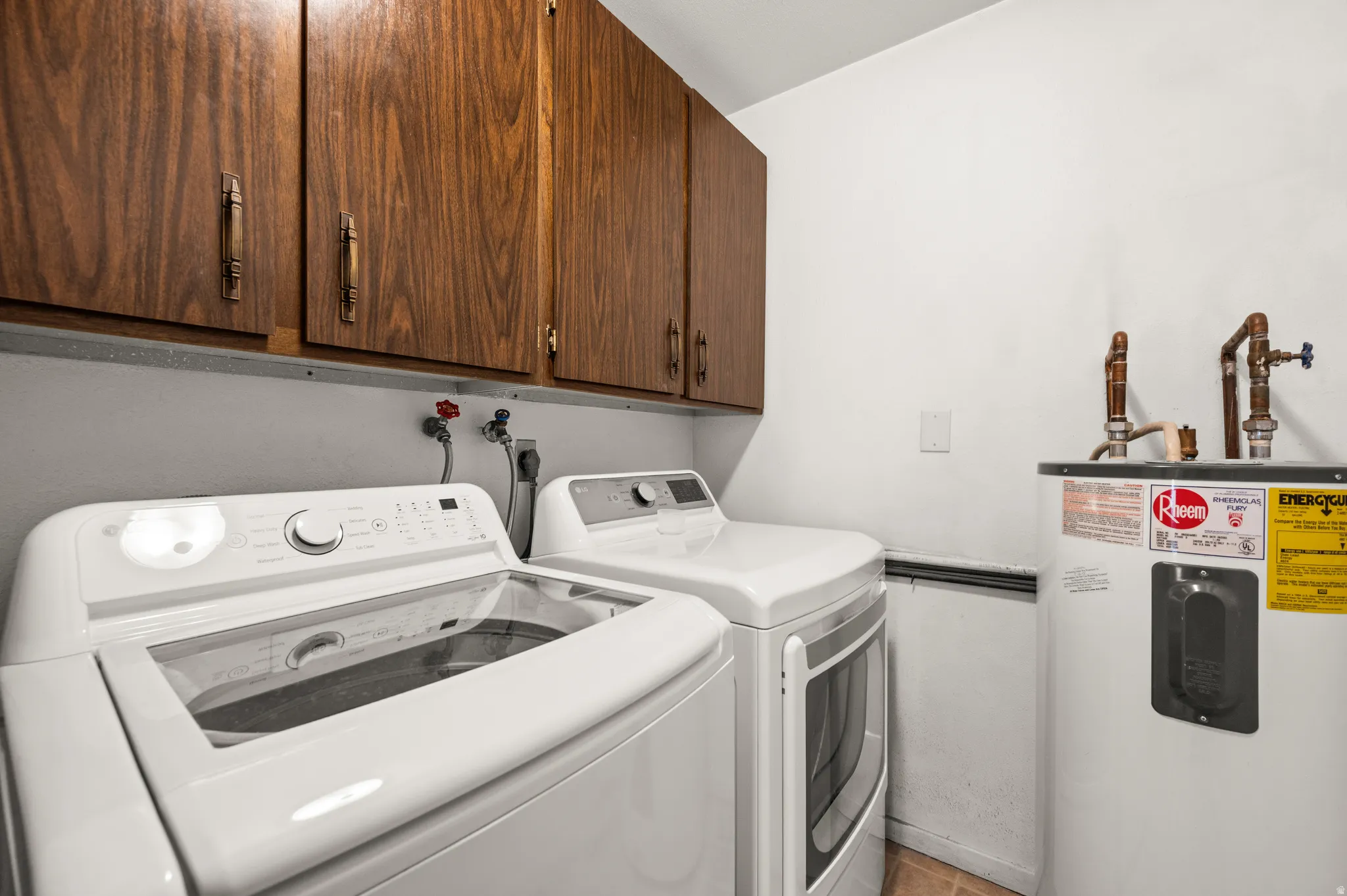 Laundry area featuring electric water heater, independent washer and dryer, and cabinet space