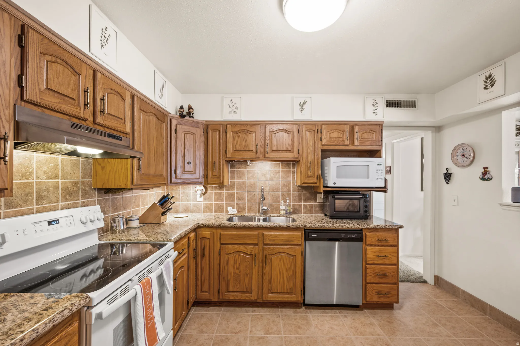 Kitchen featuring white appliances, wood finish cabinets, light stone counters, and backsplash