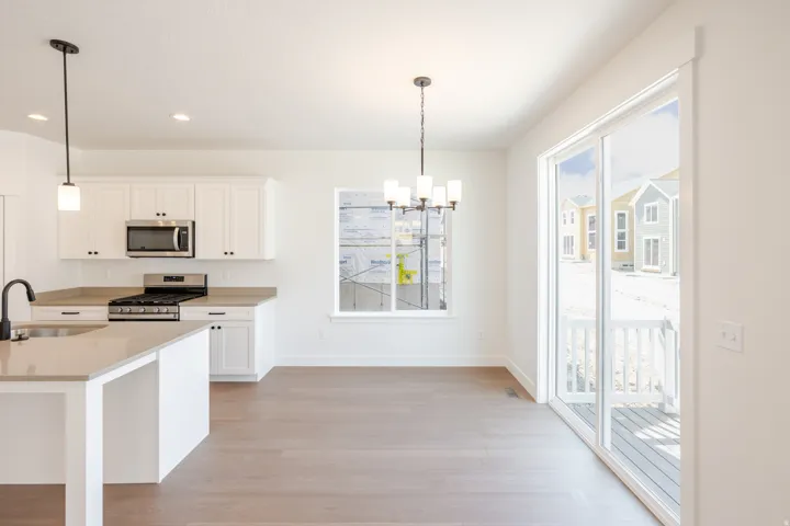 Kitchen and dining area featuring white cabinetry, stainless steel appliances, a kitchen island with sink, wood-finish flooring, and a sliding glass door to an outdoor deck