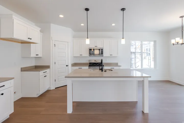 Open-concept kitchen featuring an island with a sink, white cabinetry, integrated stainless steel appliances, and wood-finish flooring