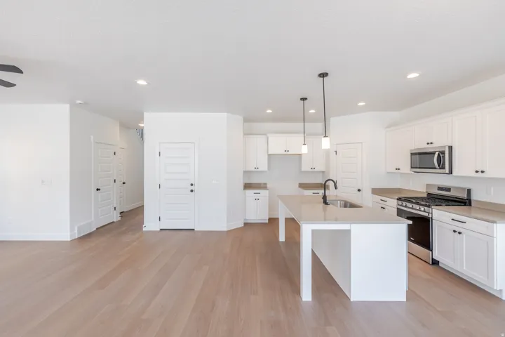 Open-concept kitchen featuring white shaker cabinetry, stainless steel appliances, a center island with sink and pendant lighting, and light wood-finish flooring