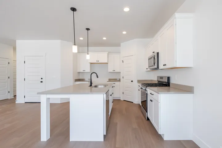 Modern kitchen featuring an island with integrated sink, white cabinetry, stainless steel appliances, pendant lighting, and wood-finish flooring