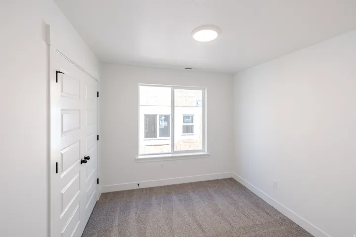 Bright room featuring a prominent window, white walls, and neutral carpeting