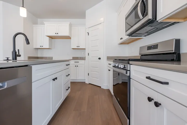 Modern kitchen featuring white shaker cabinetry, stainless steel appliances, dark countertops, and wood-finish flooring