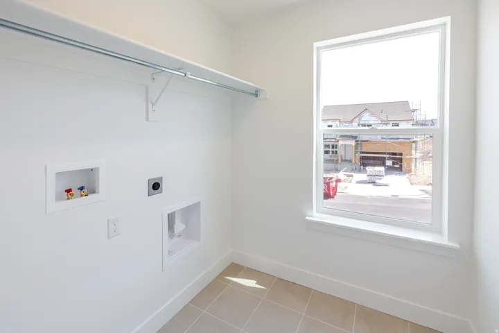 Dedicated laundry area featuring a single window, white walls, and light-toned tile flooring