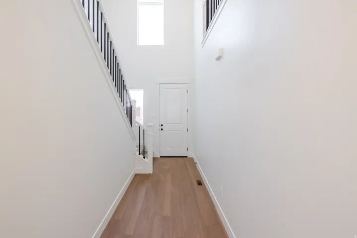 Two-story entryway featuring wood-finish flooring, a white paneled door, and a staircase with black metal balusters and white risers