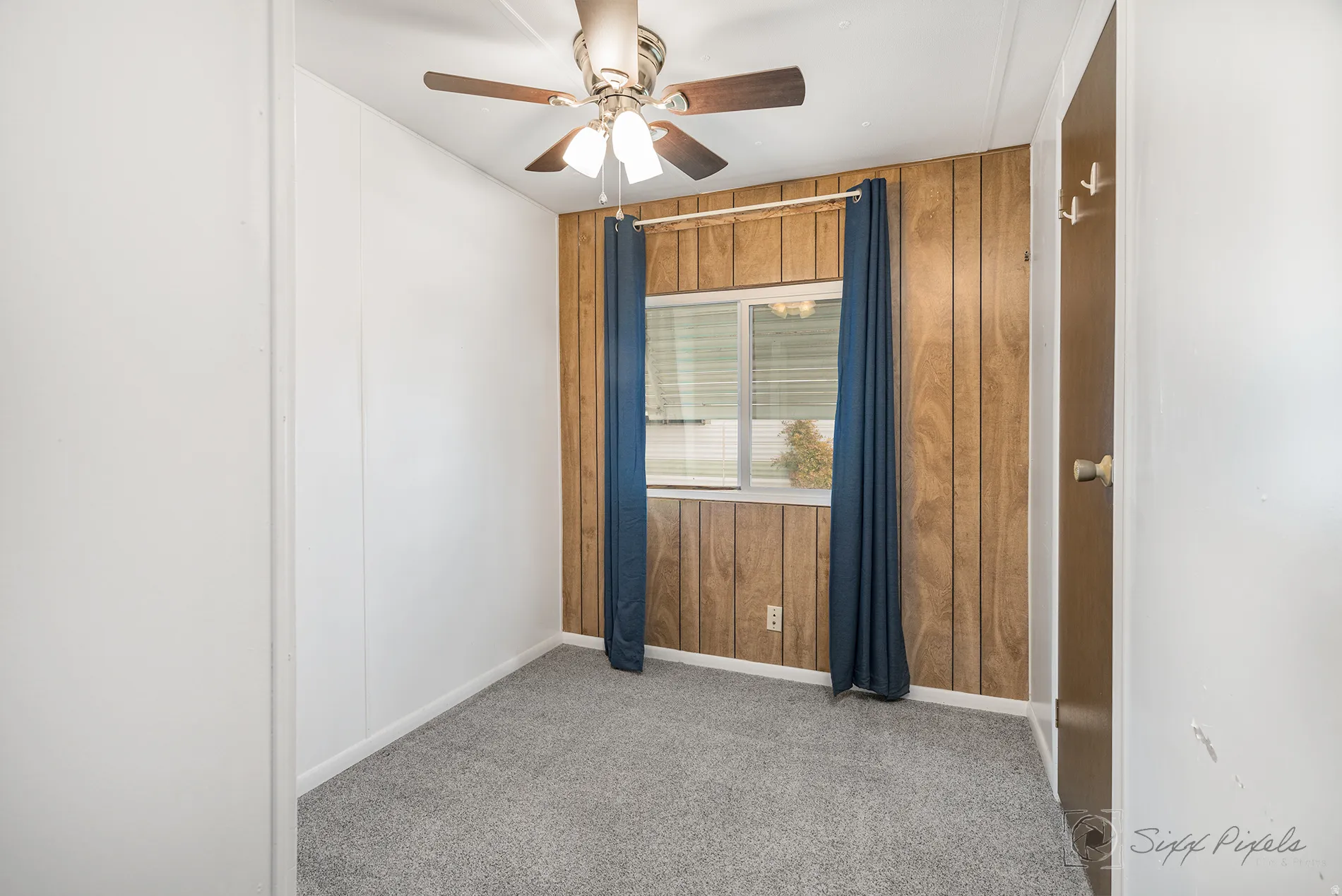 Unfurnished room with wooden walls, a ceiling fan, and light carpet