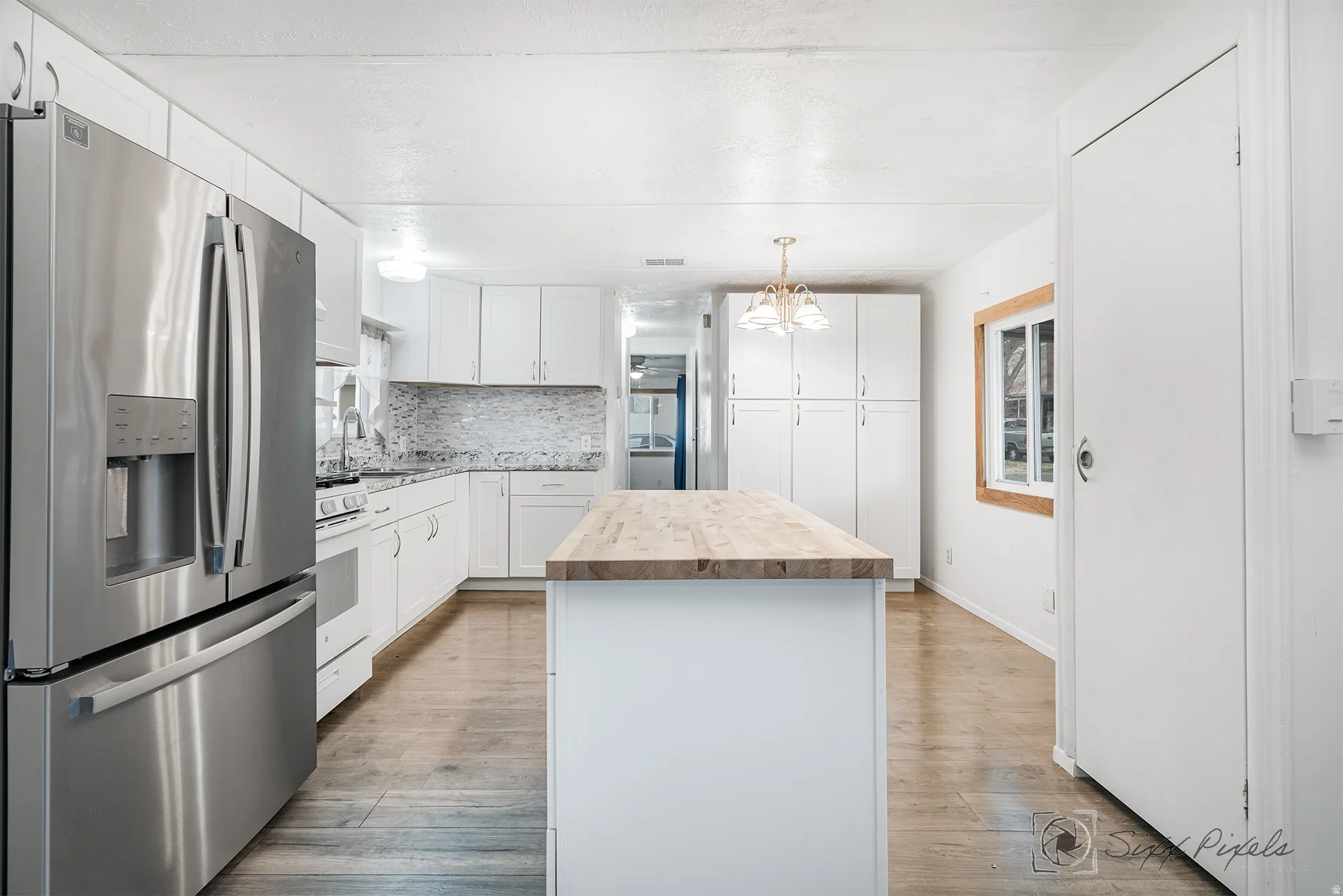 Kitchen with stainless steel refrigerator with ice dispenser, a center island, butcher block countertops, white cabinetry, and light wood-style floors