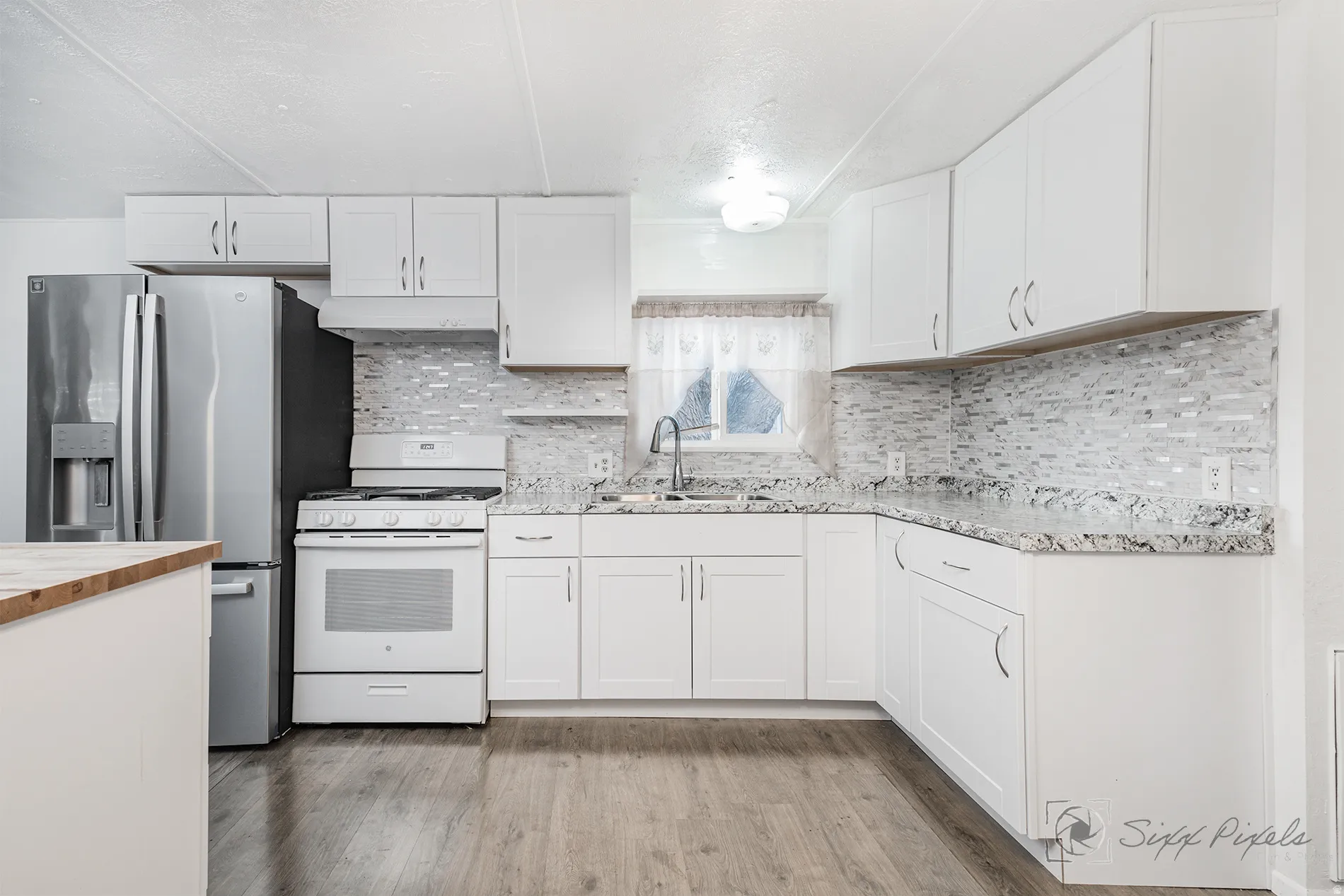 Kitchen with white cabinetry, white gas range oven, stainless steel fridge, light wood-style flooring, and backsplash