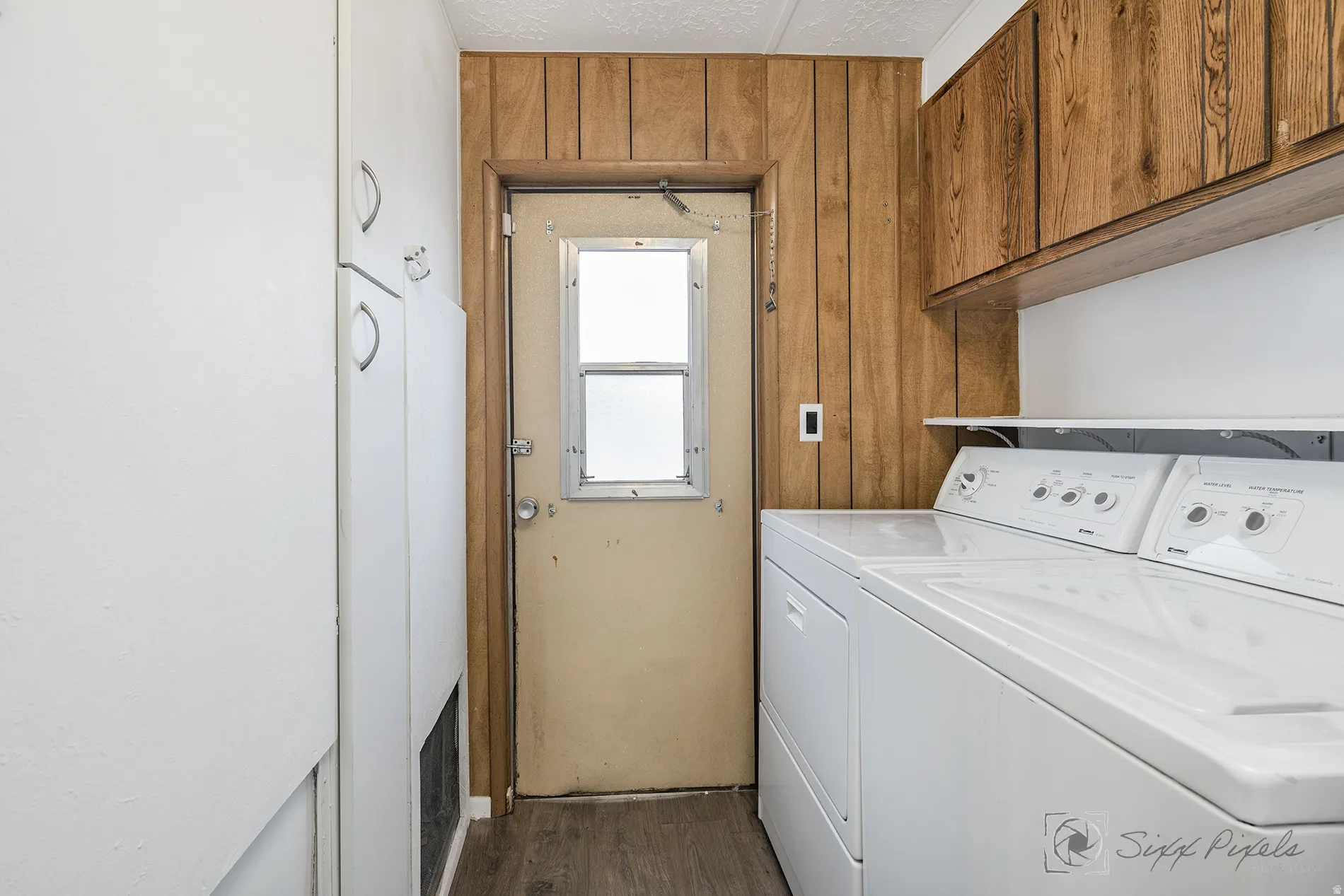 Laundry area featuring washing machine and dryer, cabinet space, wood walls, and dark wood-style floors