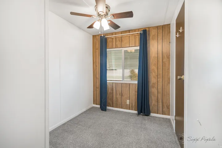 Unfurnished room with wooden walls, a ceiling fan, and light carpet