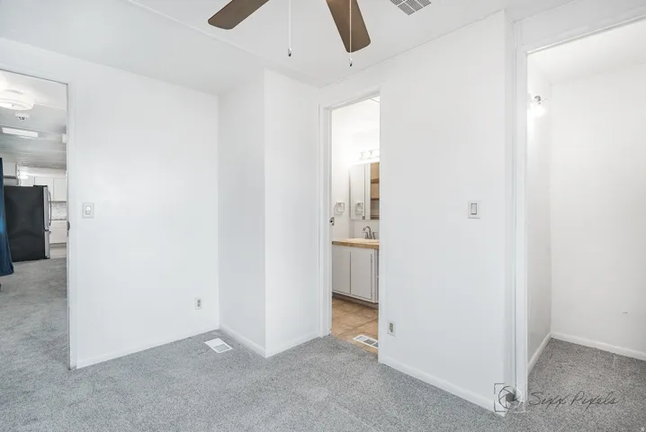 Unfurnished bedroom featuring light carpet, freestanding refrigerator, and ceiling fan