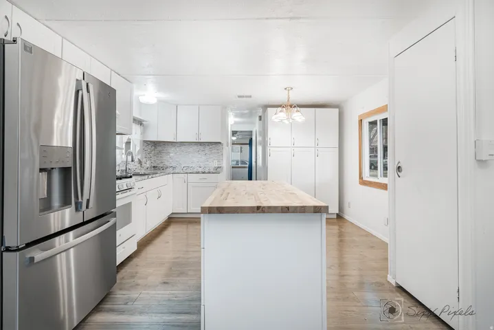 Kitchen with stainless steel refrigerator with ice dispenser, a center island, butcher block countertops, white cabinetry, and light wood-style floors