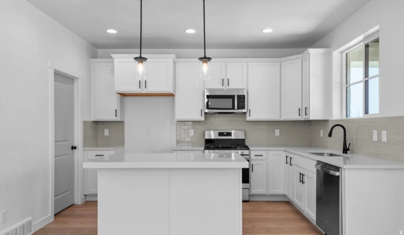 Kitchen featuring stainless steel appliances, white cabinets, a center island, and light wood-style flooring
