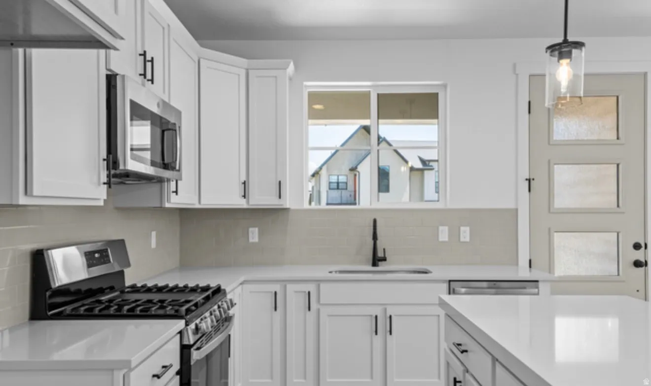 Kitchen featuring white cabinets, stainless steel appliances, decorative light fixtures, backsplash, and light stone counters