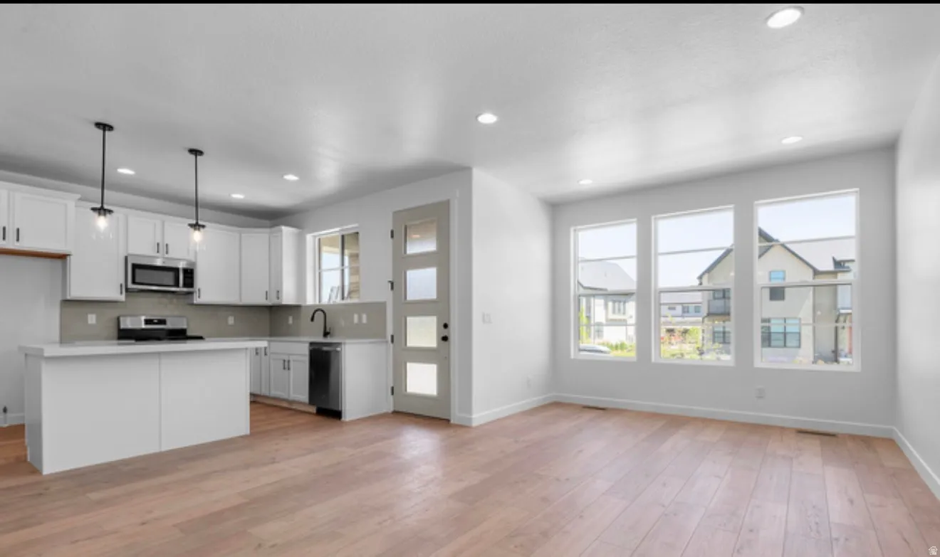 Kitchen with light countertops, open floor plan, a kitchen island, white cabinetry, and stainless steel appliances