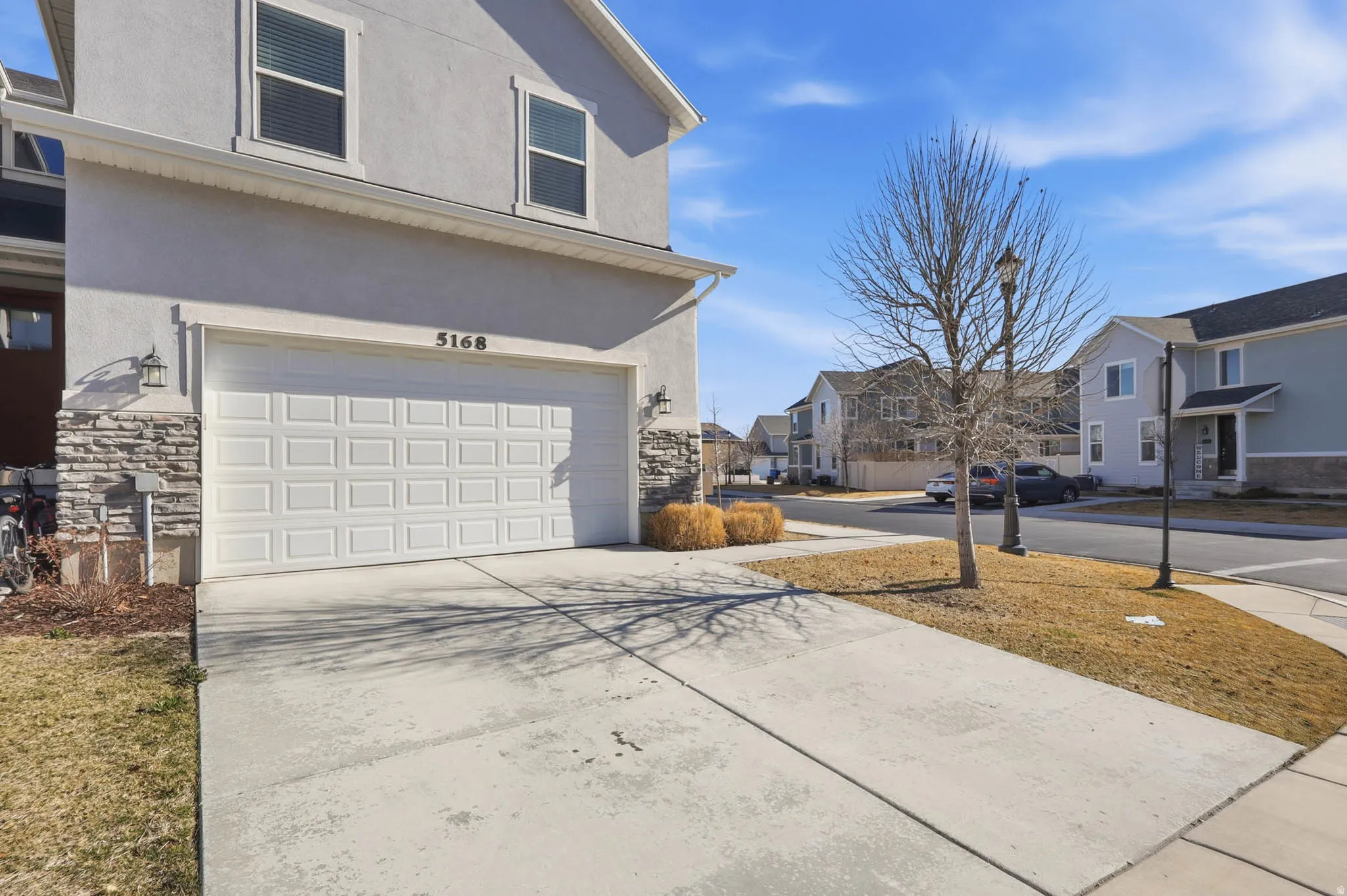 View of side of property featuring a residential view, stucco siding, driveway, a garage, and stone siding