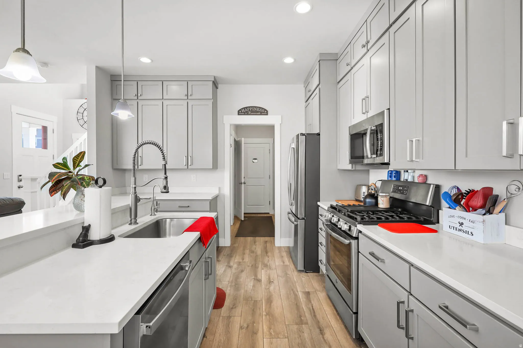 Kitchen featuring gray cabinetry, stainless steel appliances, light wood finished floors, and hanging light fixtures