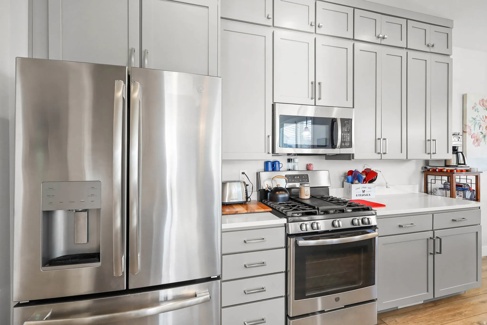 Kitchen with stainless steel appliances, light countertops, gray cabinetry, and light wood-style flooring