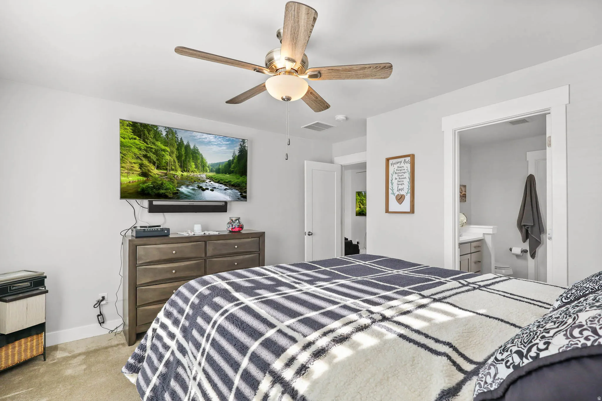 Bedroom featuring ceiling fan, light colored carpet, and ensuite bath