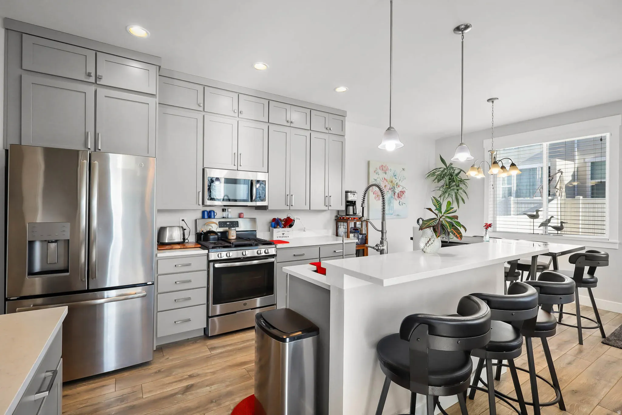Kitchen featuring gray cabinetry, stainless steel appliances, a kitchen island with sink, light wood-type flooring, and a breakfast bar area