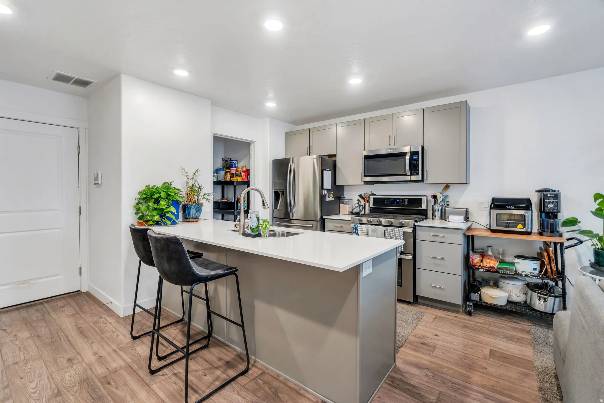Kitchen featuring gray cabinets, stainless steel appliances, a kitchen bar, light wood-style floors, and recessed lighting