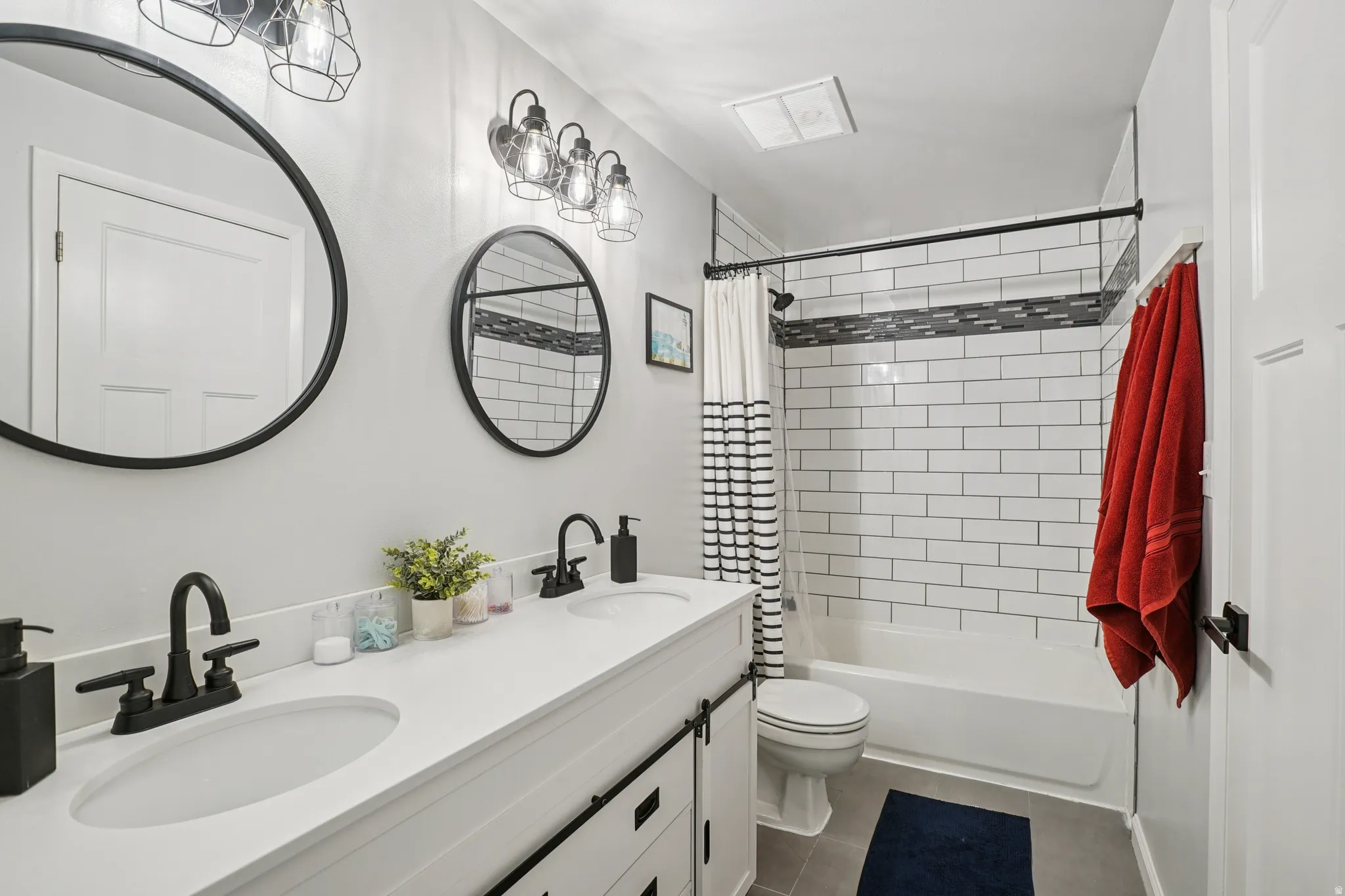 Full bath with double vanity, shower / bath combo, and dark tile patterned floors