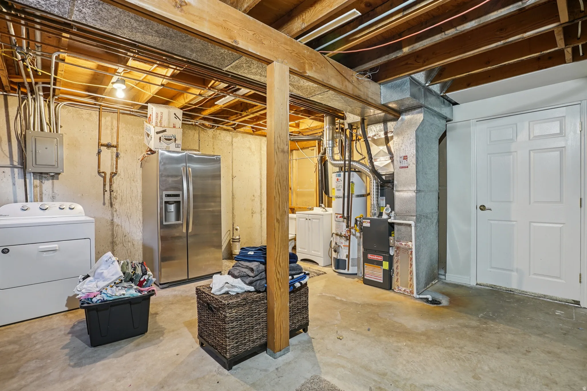 Unfinished basement featuring washer / dryer, stainless steel fridge with ice dispenser, water heater, heating unit, and electric panel
