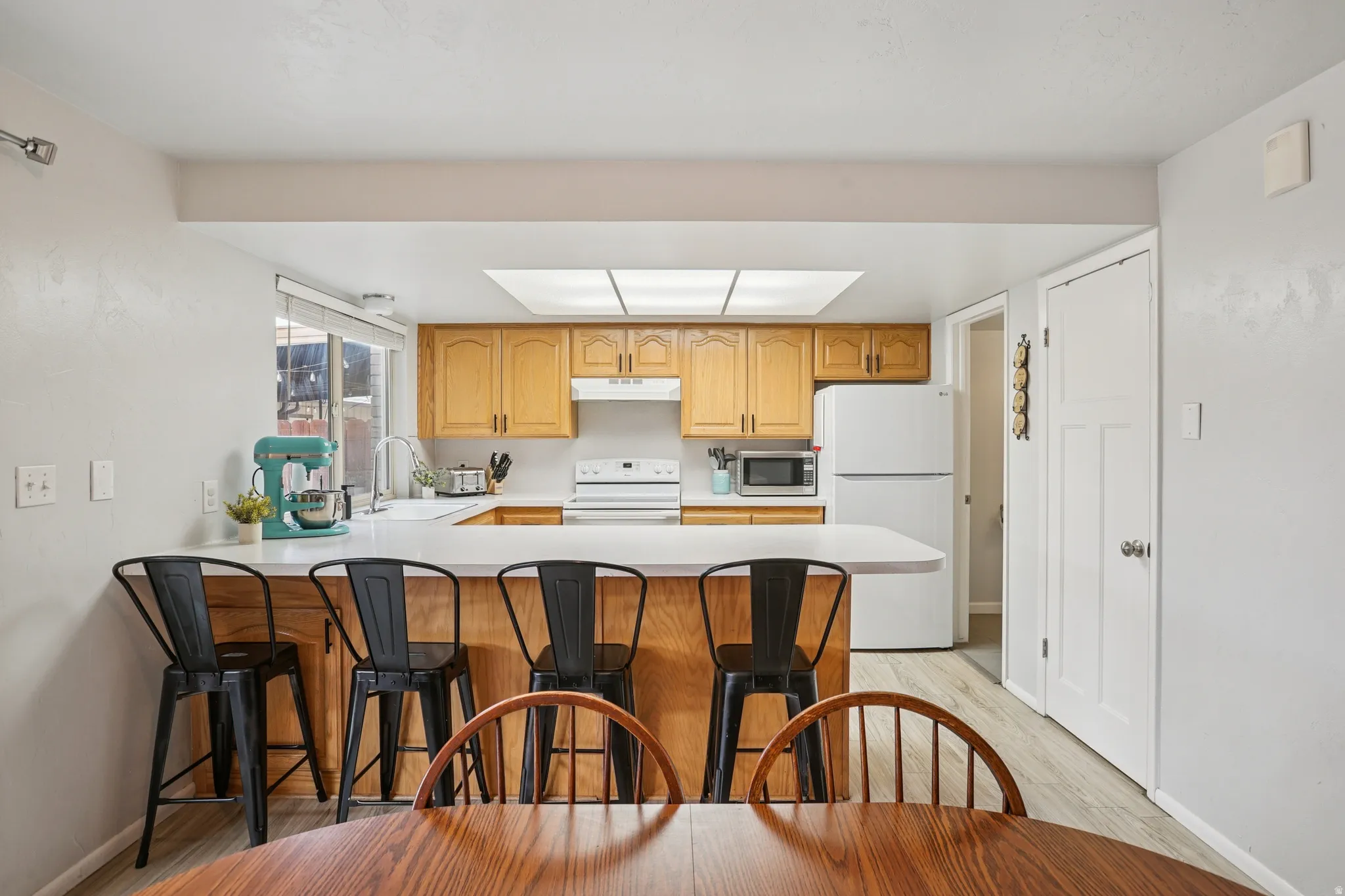 Kitchen with light countertops, white appliances, a peninsula, light wood finished floors, and a kitchen bar