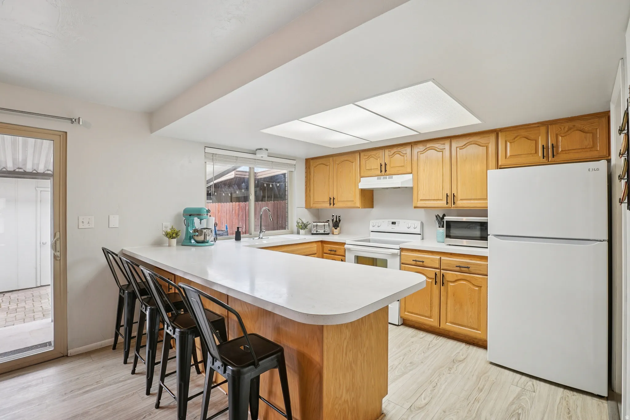 Kitchen featuring a peninsula, a breakfast bar area, white appliances, light wood-style floors, and light countertops