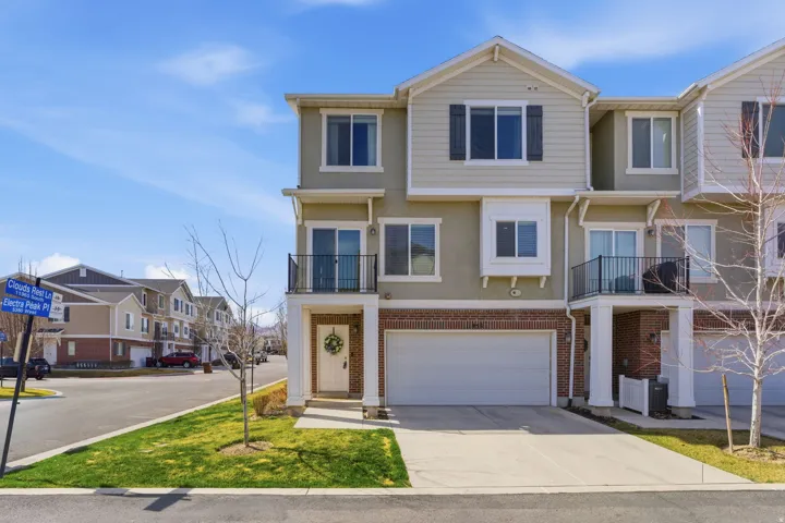 View of front of house featuring a balcony, a residential view, brick siding, driveway, and a garage