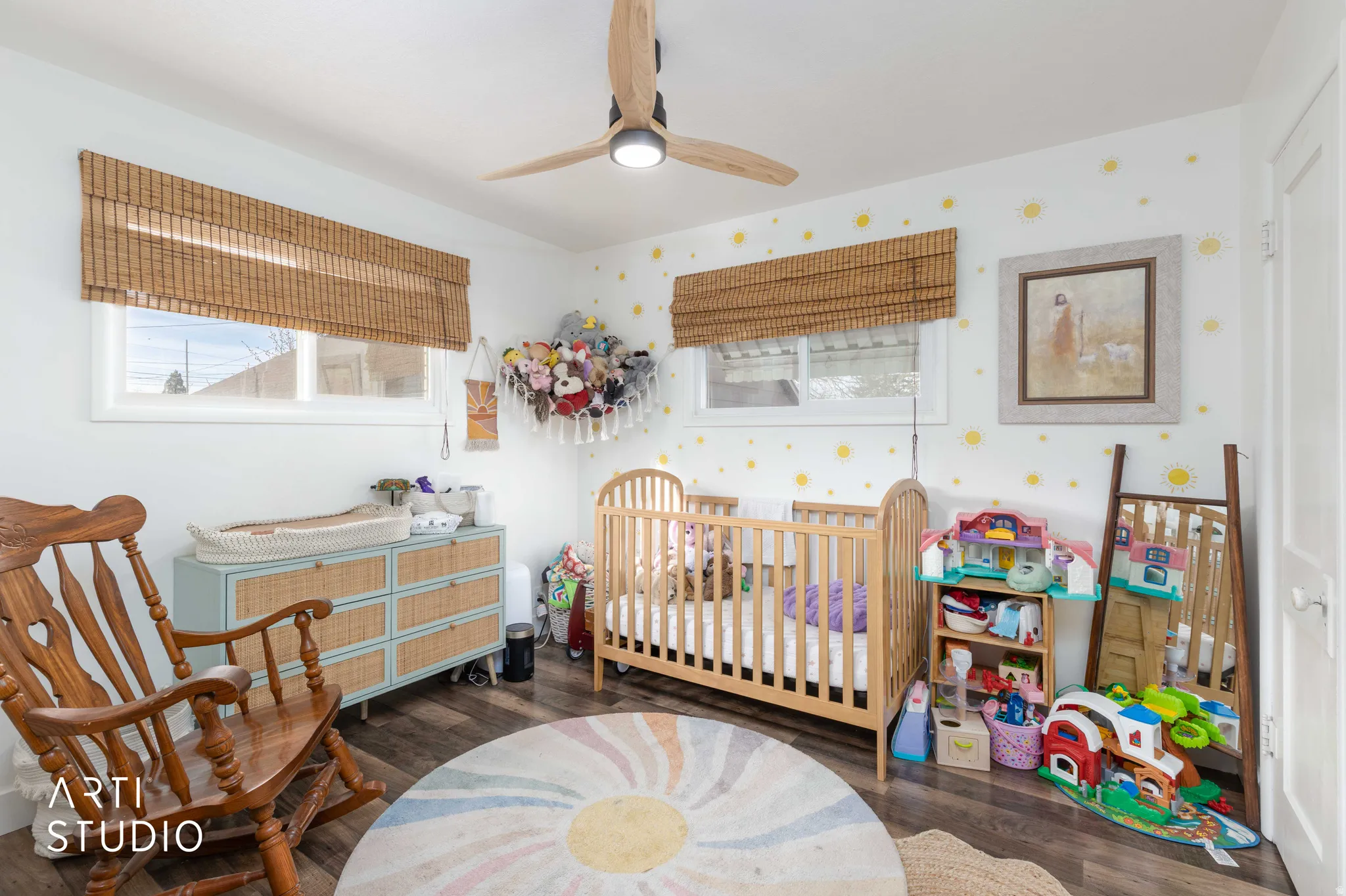 Bedroom featuring dark wood-style floors, a nursery area, a ceiling fan, and wallpapered walls