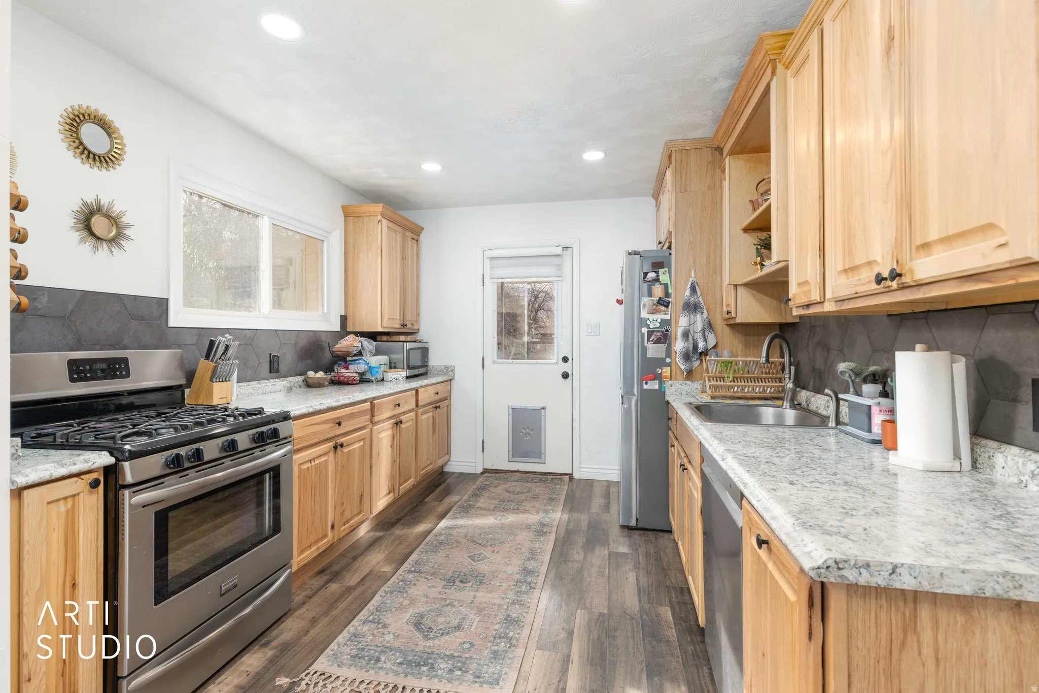 Kitchen featuring decorative backsplash, light wood finish cabinets, stainless steel appliances, open shelves, and dark wood-style flooring