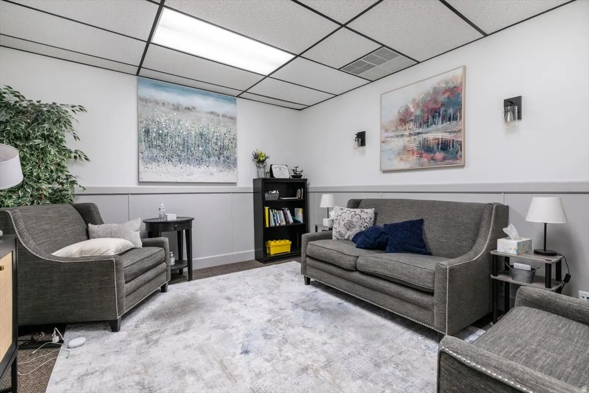 Living area with a paneled ceiling, a wainscoted wall, and carpet
