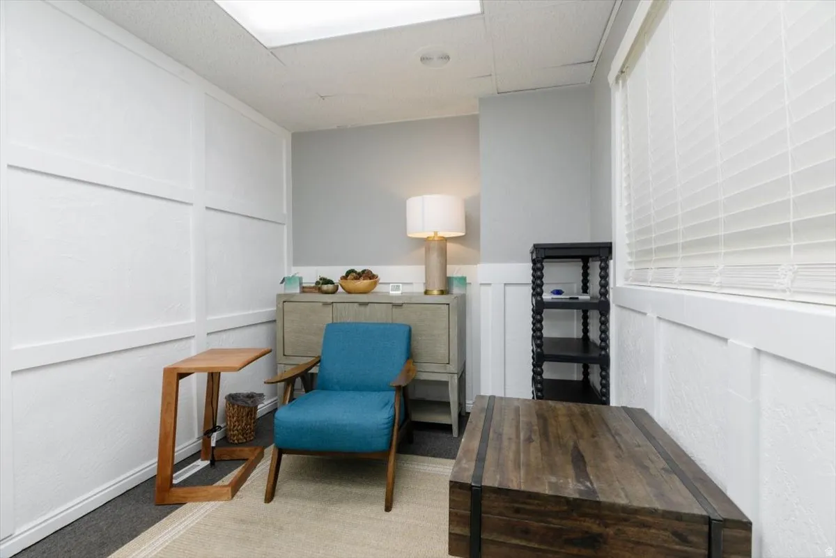 Living area with a decorative wall, light colored carpet, a drop ceiling, and wainscoting