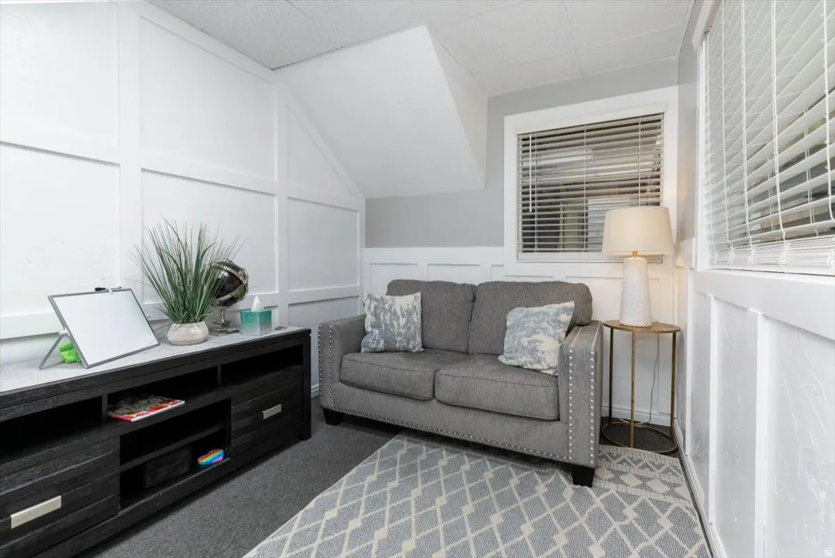 Living area with a decorative wall, vaulted ceiling, and carpet floors